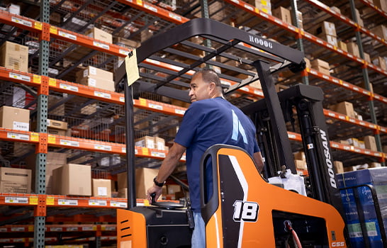 Essendant - Warehouse Employee on Forklift Drives Through Warehouse Stacks
